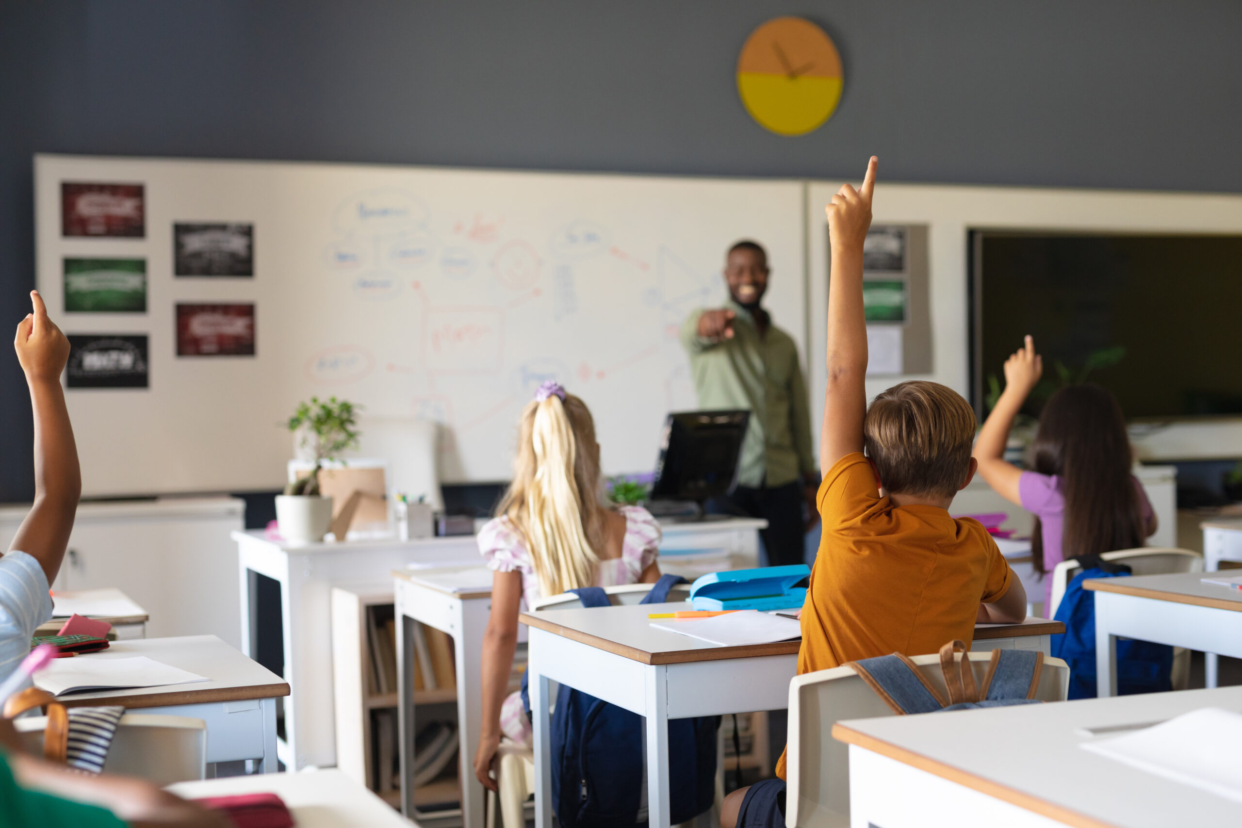 African american young male teacher pointing on multiracial elementary students with hand raised. unaltered, education, learning, childhood, teaching, occupation and school concept.